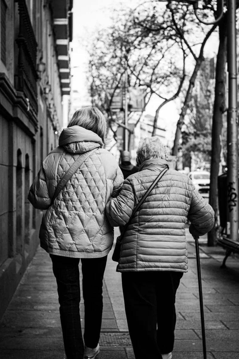 Two older women walking arm in arm down a city sidewalk