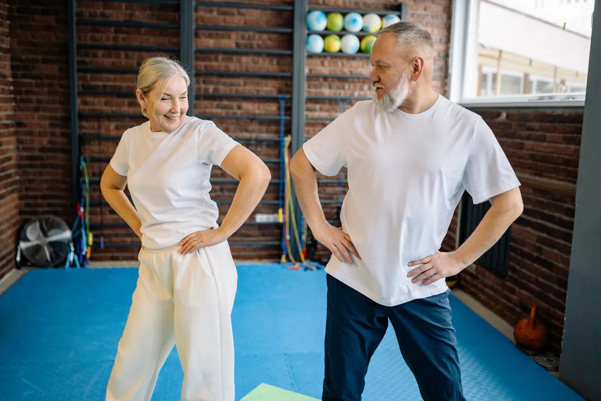 An older woman and man stretching together in a bright exercise studio
